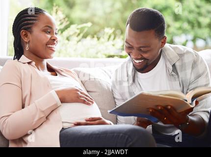 Story time. a handsome young man reading a book to pregnant wifes belly while sitting on the sofa at home. Stock Photo