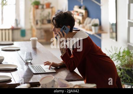Young female pottery business owner using laptop talking with client by phone, checking online order Stock Photo