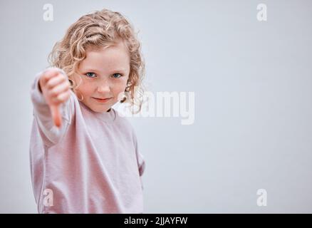 No fair. Studio shot of a little girl showing thumbs down against a grey background. Stock Photo