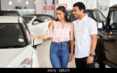 I think we can both agree that this is the car for us. a young couple looking at cars at a car dealership. Stock Photo