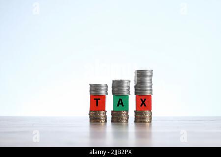 Words on TAX are written on the wooden blocks sandwiched with stacks of coins Stock Photo
