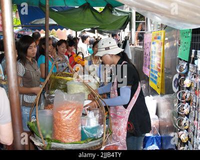 Bangkok Thailand - August 10 2007; Busy city street lined with market food products and clothes for sale crowded with tourists and locals. Stock Photo