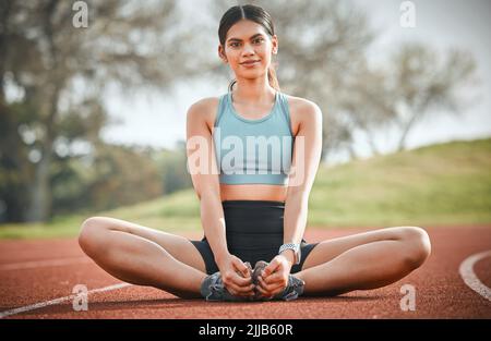 I came out here to win today. Portrait of a young athlete stretching her body on a running track. Stock Photo