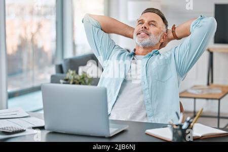 The joys of being an entrepreneur. a mature businessman sitting alone in his home office with his hands behind his head in relief. Stock Photo