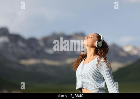 Relaxed woman wearing wireless headphones meditating listening audio guide in a high mountain