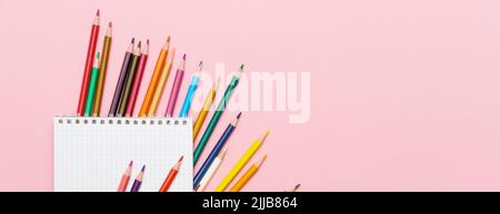 Colored pencils for drawing and a notebook in a cage on a pink background. Back to school concept Stock Photo