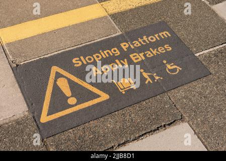 St Erth, Cornwall, England, UK. 2022. Warning sign  of a sloping platform surface to passengers using wheelchairs, trolleys and pushchairs at St Erth Stock Photo