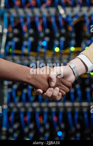 Close-up of server engineers shaking hands during teamwork in server room Stock Photo
