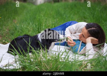 Woman with her dog relaxation outdoors together. Pet owner and her border collie laying on blanket at park Stock Photo