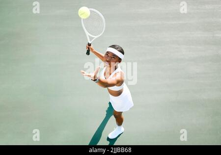 Theres power in her swing. a young woman serving a ball while playing tennis on a court. Stock Photo
