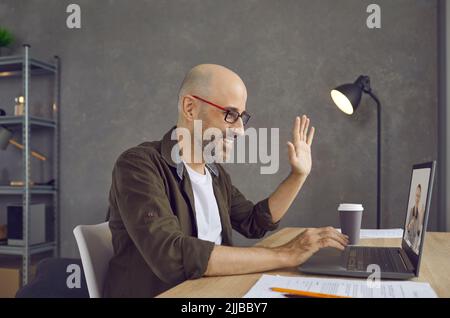 Man starting virtual business meeting and waving hello at screen of laptop computer Stock Photo