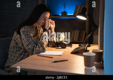 Fatigued asian woman student suffering eyestrain using tablet pc complaining at night at home. tired stressed young college girl massage nose bridge Stock Photo