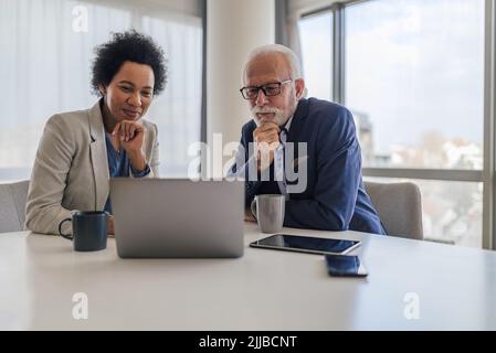 Focused male and female partners analyzing business plan on laptop. Colleagues sitting with hand on chin during meeting at desk. They are brainstormin Stock Photo