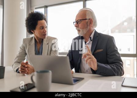 Serious male and female professionals discussing business strategy on laptop. Partners planning strategy during meeting at desk. They are working toge Stock Photo