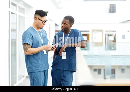 Portrait of two multiethnic doctors wearing uniform standing in hall of modern clinic nd chatting, copy space Stock Photo
