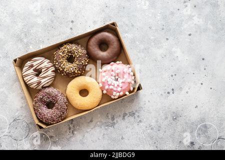 Different donuts with  chocolate frosted, pink glazed and sprinkles into the box on grey  background with copy space. Assortment of various colorful d Stock Photo