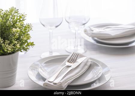 Table setting white and grey colour. Empty glasses and plates set with napkin and cutlery. Restaurant interior background. Stock Photo