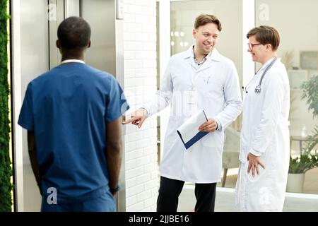 Group of cheerful doctors waiting for elevator in modern hospital building Stock Photo