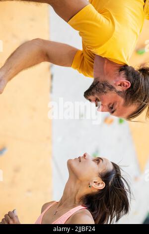 Man and woman on the background of an artificial climbing wall. The man hangs upside down at the level of the girl's head. Stock Photo