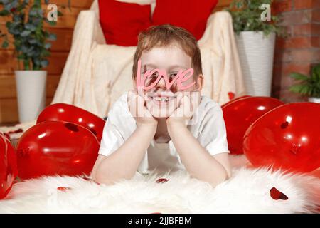 Valentine's Day children or kids. Cute joyful little boy with red balloons in the shape of a heart and text love in the form of glasses, on Valentine' Stock Photo
