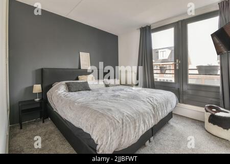 Comfortable bed with ornamental blanket placed near glass door and wardrobe with mirror in light bedroom Stock Photo