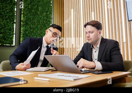 Portrait of two business professionals discussing strategies in meeting and using laptop Stock Photo