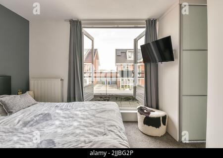 Comfortable bed with ornamental blanket placed near glass door and wardrobe with mirror in light bedroom Stock Photo