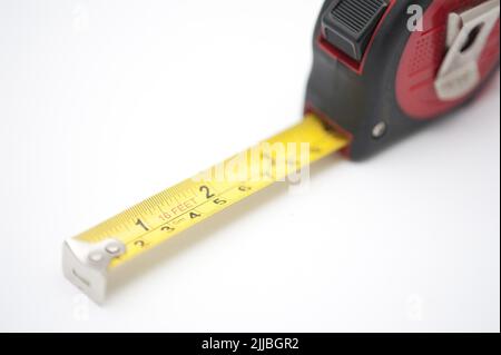 Builders retractable tape measure with centimeters and inches on a white background with part of the tape extended to show the two scales Stock Photo