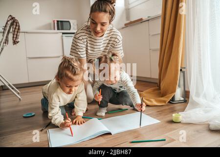 Woman sitting on the kitchen floor with her creative children Stock Photo