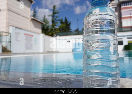 A bottle of cold mineral water with condensation droplets on the walls on a hot day on the edge of the pier on a blurred background of the sea.Close u Stock Photo