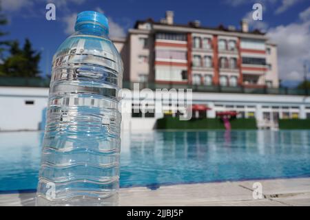 A bottle of cold mineral water with condensation droplets on the walls on a hot day on the edge of the pier on a blurred background of the sea.Close u Stock Photo