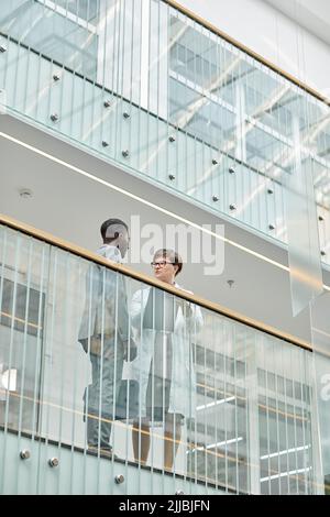 Graphic low angle portrait of two business people standing at balcony in modern office building with glass elements Stock Photo