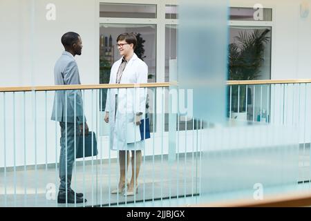 Full length shot of two people, man and woman chatting while standing at balcony in modern office building with glass decor, copy space Stock Photo