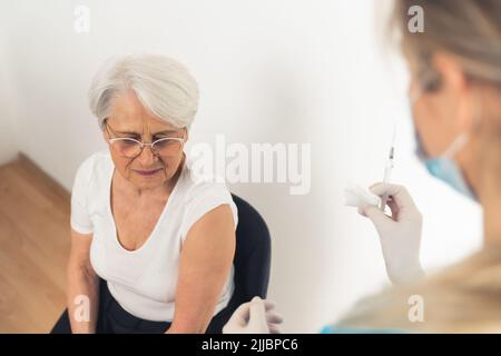 A nurse holding a syringe and a cotton pad, getting ready to give a vaccination shot to an elderly woman. High quality photo Stock Photo