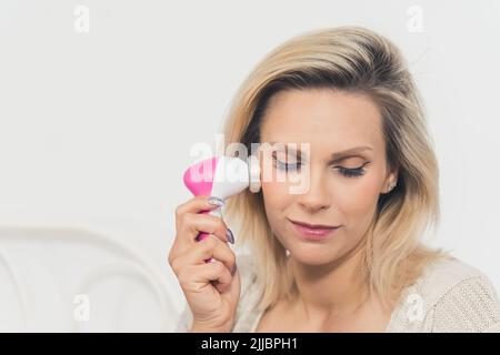 Closeup portrait of a European woman doing her skin care routine. Beautiful blonde caucasian middle-aged girl using a face massager. High quality photo Stock Photo