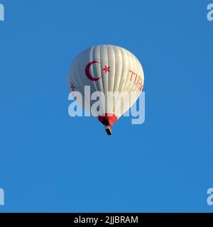 GOREME/TURKEY - June 27, 2022: hot air balloon with turkey flag flies in the blue sky Stock Photo