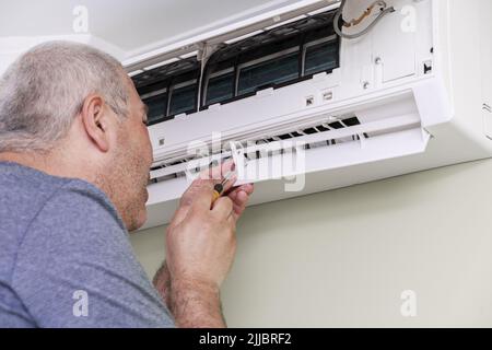 man using screwdriver to repairing air conditioner indoors Stock Photo