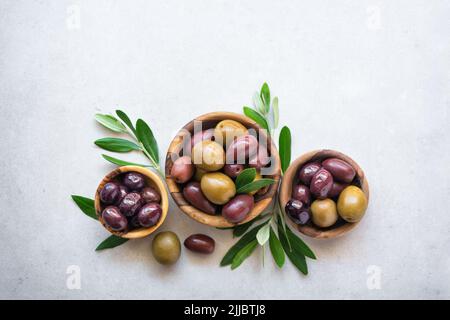 Tasty olives in wooden bowls with green branches on light background Stock Photo
