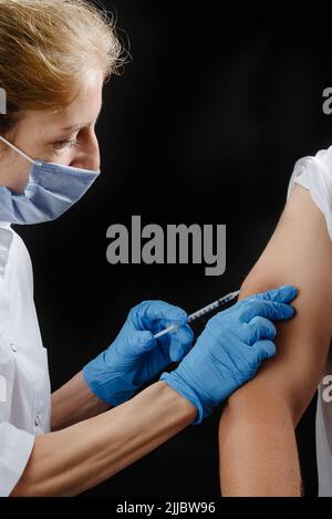 the doctor gives the shot in his hand on a black background. A female nurse vaccinates a patient Stock Photo