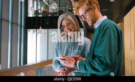 Diverse friendly coworkers talking using digital tablet, discussing project.  Stock Photo