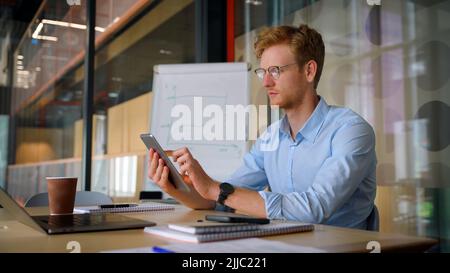 Young ethnic successful businessman holding tablet sitting in office. Stock Photo