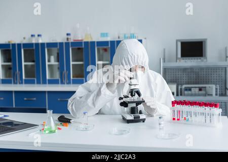 Scientist in hazmat suit using microscope near test tubes with monkeypox lettering in lab Stock Photo