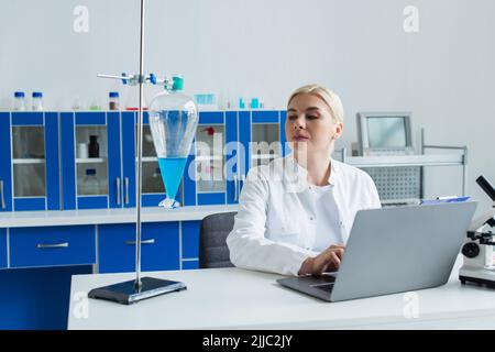 Scientist using laptop and looking at flask with liquid in laboratory Stock Photo