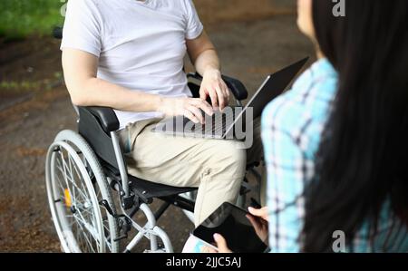 Man in wheelchair and woman work remotely while sitting in park Stock Photo