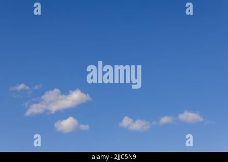 Small white cumulus clouds drift across the lower part of a blue spring sky in Trentino, Italy, leaving broad copy space above. Stock Photo