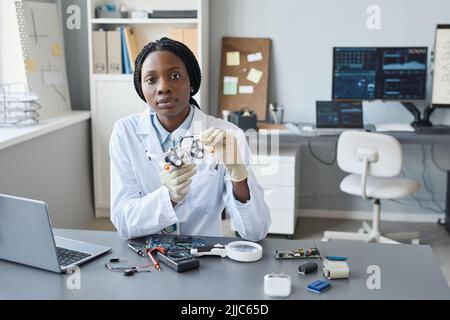 Portrait of young female scientist looking at camera while sitting at workplace in engineering lab, copy space Stock Photo