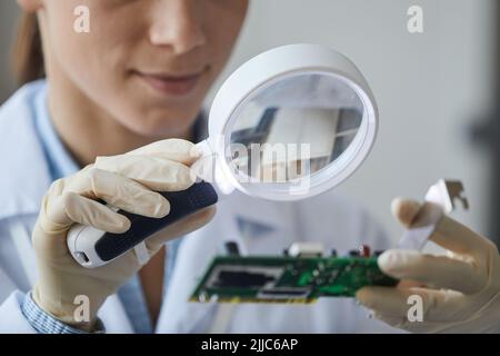 Close up of young woman holding magnifying glass in engineering laboratory, copy space Stock Photo