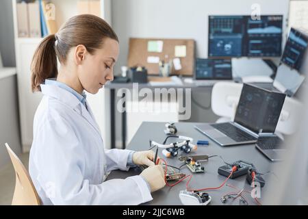 Side view portrait of female lab technician checking hardware parts at quality control station, copy space Stock Photo