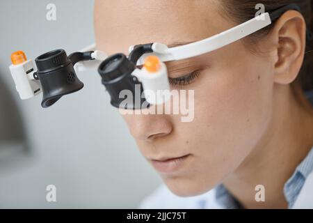 Close up of young female scientist wearing magnifying visor in laboratory Stock Photo