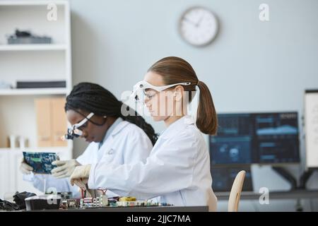 Side view portrait of two female engineers working with electronic parts in laboratory, copy space Stock Photo
